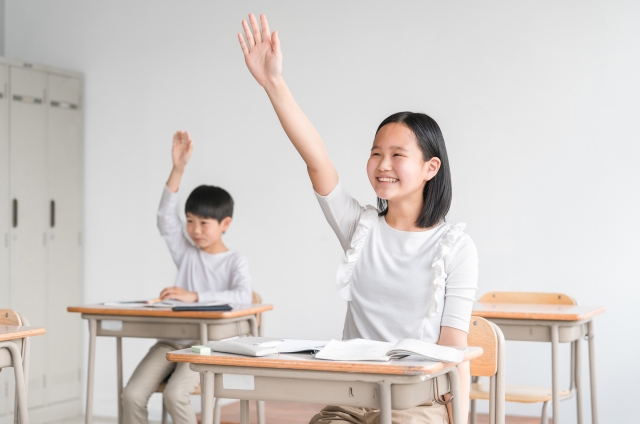 学校の授業中に挙手をするこどもたち