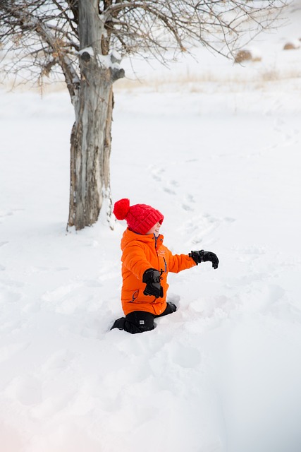 赤いダウンジャケットを着た子供が雪山で遊んでいる