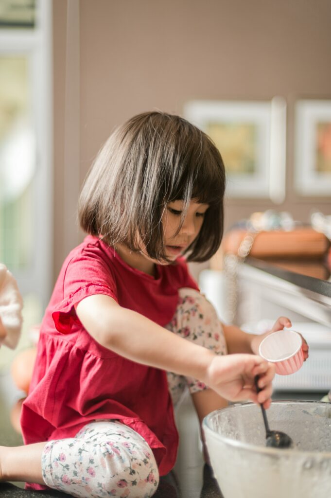 料理のお手伝いをしている、おたまとケーキカップを持った幼い女の子