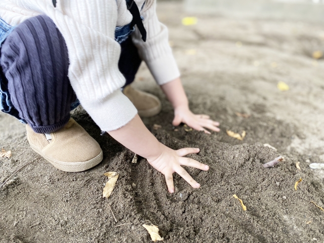 砂場の砂に両手をつく子供