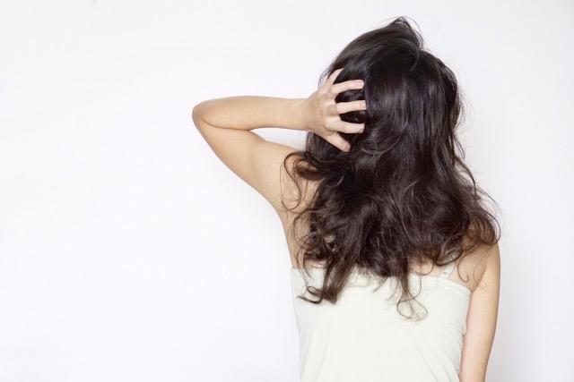 頭を抱える、痛んだ髪の女性の後ろ姿