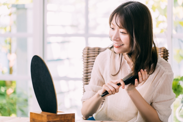 鏡を見ながらヘアブラシで髪をといて笑う女性